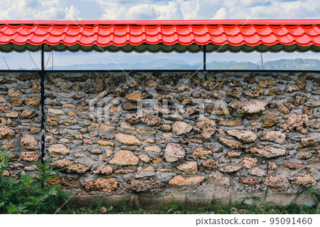 Old style wall made of rough stones with cement. Ancient grunge stones wall backdrop. Background of old vintage wall. Stone fence with red roof decoration to be beautiful and strong with natural stone 95091460