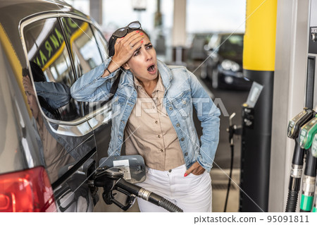 Woman refuelling the tank of her car with diesel looks shocked with mouth open seeing the high price of fuel 95091811