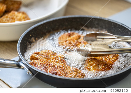 Detail of pan with schnitzels bubbling in hot oil and pliers taking them out Detail of pan with schnitzels bubbling in hot oil and pliers taking them out 95092120