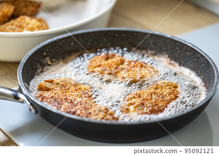 Sizzling hot oil with schnitzel frying in it in a dark pan 95092121