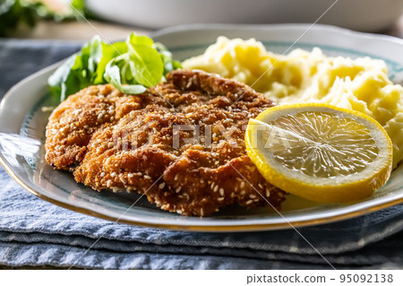 Tasty fried schnitzel served with mashed potatoes and greens with a slice of lemon 95092138