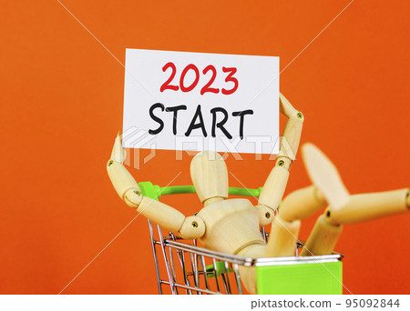 2023 Start symbol. White paper with words 2023 Start, human model in shopcart. Beautiful orange table orange background. Business and 2023 start concept. Copy space. 95092844
