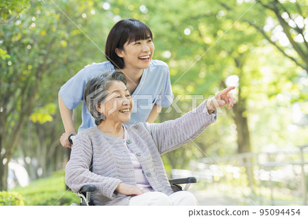 Female healthcare worker pushing senior woman's wheelchair 95094454