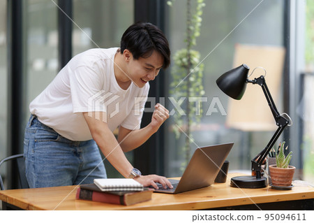Happy Asian man using laptop computer while have a good news working at office Happy Asian man using laptop computer while have a good news working at office 95094611