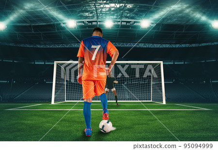 Soccer scene at night match with player in orange uniform kicking the penalty kick Soccer scene at night match with player in orange uniform kicking the penalty kick 95094999
