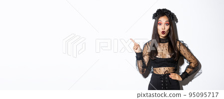 Surprised attractive asian woman in witch outfit pointing finger at upper left corner, showing halloween advertisement, promo of party. Beautiful female in black gothic dress looking amazed Surprised attractive asian woman in witch outfit pointing finger at upper left corner, showing halloween advertisement, promo of party. Beautiful female in black gothic dress looking amazed 95095717