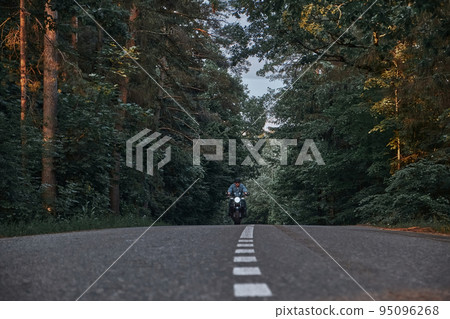 Blurred Motion A young man biker in a helmet quickly rides at high speed on a forest road, in motion 95096268