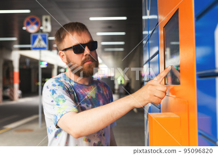 Man enters parcel code on screen and picks up parcel from automated postal machine. Man enters parcel code on screen and picks up parcel from automated postal machine. 95096820