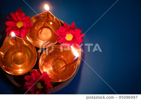 Happy Diwali. Celebrating the Indian Festival of Light. Traditional diya oil lamps and red flowers on blue background 95096997
