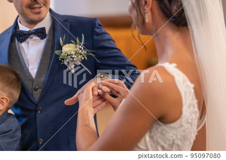 Bride puts a ring on a finger of a groom during a wedding ceremony, becoming husband and wife 95097080