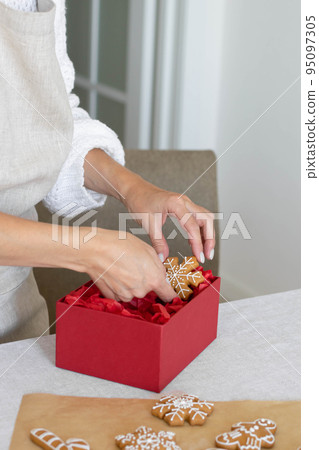 Woman puts traditional gingerbread cookies with icing into a festive box. Home traditions and gifts 95097305