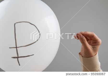 Caucasian woman pops a balloon with a ruble inscription with a needle.  95098067