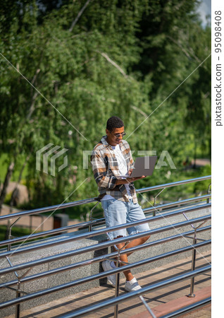 A man with a laptop working outside and looking involved A man with a laptop working outside and looking involved 95098408