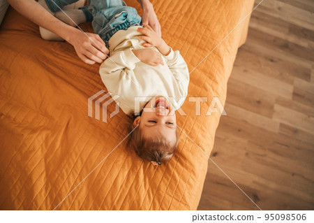 Adorable fair-haired little girl laughing in the bedroom Adorable fair-haired little girl laughing in the bedroom 95098506