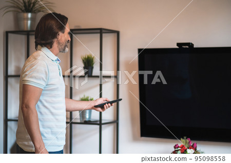 Man in a white thsirt spending time at home and switching on tv Man in a white thsirt spending time at home and switching on tv 95098558