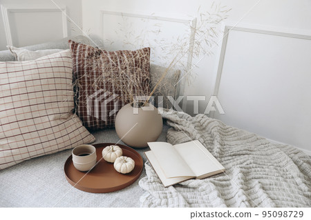 Breakfast in bed, sofa stationery mockup scene. Cup of coffee, pumpkins. Open book. Cup of coffee on tray. Dry grass bouquet in ball shaped vase on linen throw. Lifestyle concept. Checkered cushions. 95098729