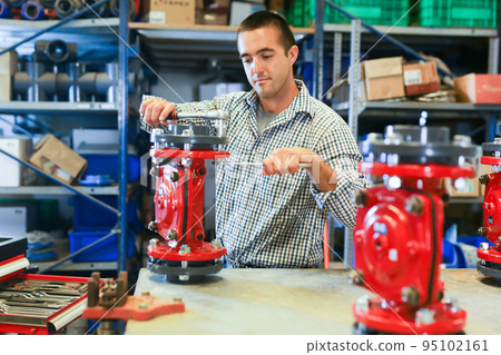 Factory worker assembles shutoff valves using various tools indoor 95102161