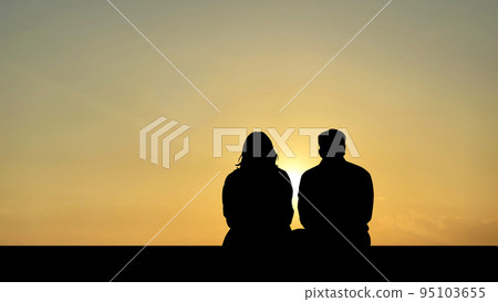 Man and woman silhouette sitting facing the setting sun 95103655