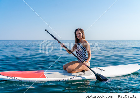 Sporty girl on a glanders surfboard in the sea on a sunny summer day. In a striped swimsuit, it is in the bar. Summer activities by Stortom by the sea 95105132
