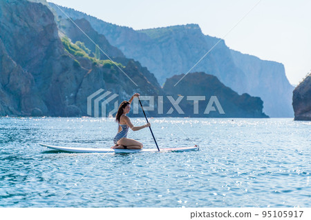 Sporty girl on a glanders surfboard in the sea on a sunny summer day. In a striped swimsuit, it is in the bar. Summer activities by Stortom by the sea Sporty girl on a glanders surfboard in the sea on a sunny summer day. In a striped swimsuit, it is in the bar. Summer activities by Stortom by the sea 95105917