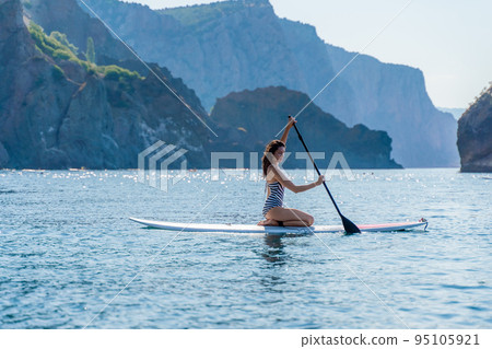 Sporty girl on a glanders surfboard in the sea on a sunny summer day. In a striped swimsuit, it is in the bar. Summer activities by Stortom by the sea 95105921