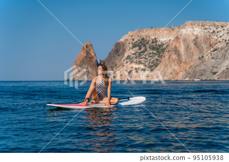 Sportive girl on a surfboard glanders in the sea on a sunny summer day. In a striped swimsuit. Summer fun from Stortom by the sea 95105938