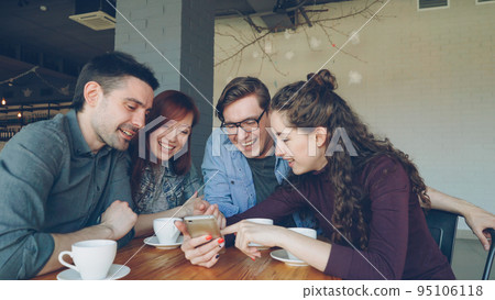 Young happy people are watching smartphone screen discussing photos and laughing during lunch break in cafe. Friendship, modern technology and modern lifestyle concept. Young happy people are watching smartphone screen discussing photos and laughing during lunch break in cafe. Friendship, modern technology and modern lifestyle concept. 95106118