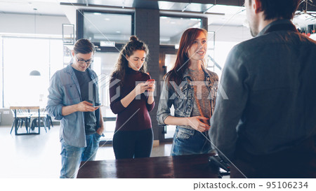 Queue of cheerful young people standing in coffee-house in the morning and buying takeaway drinks . Modern lifestyle concept. Queue of cheerful young people standing in coffee-house in the morning and buying takeaway drinks . Modern lifestyle concept. 95106234