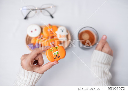 woman hand holding funny Halloween Cookie during drinking coffee. Happy Halloween day, Trick or Threat, Hello October, fall autumn, Traditional, party and holiday concept 95106972