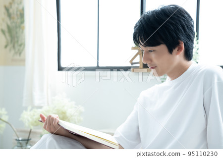 Young man relaxing and reading in his room on holiday 95110230