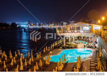 Tourists relaxing near a swimming pool at night 95110820