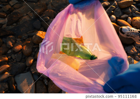 Cleaning from environmental pollution. A volunteer wearing gloves holds an open bag with plastic garbage and bottles. Close-up, top view. The concept of Earth Day and Sustainable Ecology 95111168