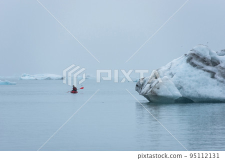 Guy kayaking among floating icebergs in Jokulsarlon, Iceland 95112131
