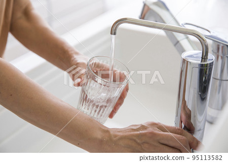 一個女人的手，她從淨水器裡把水放進杯子裡 95113582