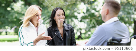Two women and a man in wheelchair communicate in park 95113606
