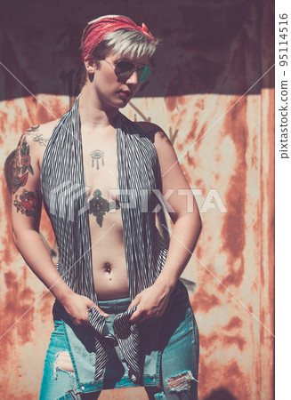 Young fashion woman with short blonde hair and red turban. Attractive girl portrait with denim shorts and sunglasses posing on the grunge metal background. Happy young female, advertisement concept Young fashion woman with short blonde hair and red turban. Attractive girl portrait with denim shorts and sunglasses posing on the grunge metal background. Happy young female, advertisement concept 95114516