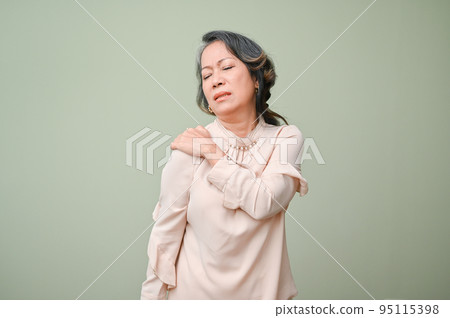 60s aged Asian woman suffering from her shoulder pain, massaging her shoulder 95115398
