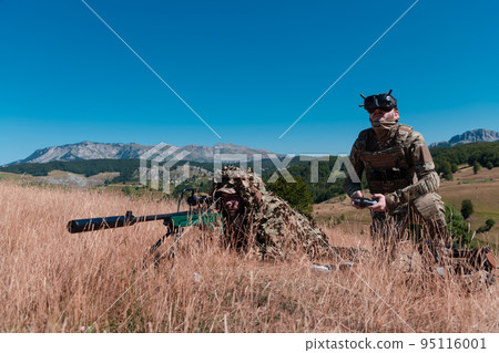 Sniper soldier assisted by an assistant to observe the area to be targeted with modern warfare tactical virtual reality goggles aerial drone military technology. Sniper soldier assisted by an assistant to observe the area to be targeted with modern warfare tactical virtual reality goggles aerial drone military technology. 95116001