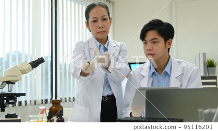 Senior female scientists analyzing test samples, discussing about new test results with young researcher in laboratory 95116201