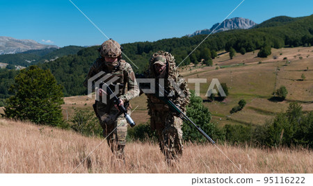 A sniper team squad of soldiers is going undercover. Sniper assistant and team leader walking and aiming in nature with yellow grass and blue sky. Tactical camouflage uniform. 95116222
