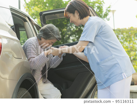 Female helper helping senior woman get out of car Female helper helping senior woman get out of car 95116311