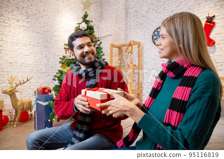 Young man giving presents for surprise girlfriend in celebration Christmas together at home. 95116819