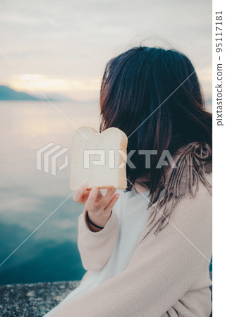 一個女人在美麗的日出中吃麵包的照片 95117181