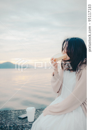 一個女人在美麗的日出中吃麵包的照片 95117183