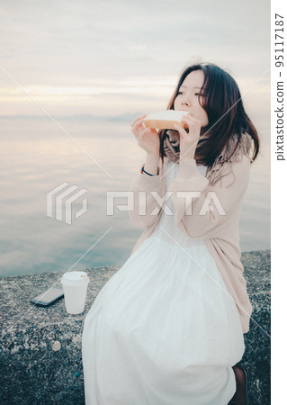 一個女人在美麗的日出中吃麵包的照片 95117187