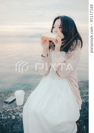 一個女人在美麗的日出中吃麵包的照片 95117188