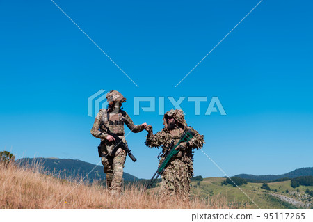 A sniper team squad of soldiers is going undercover. Sniper assistant and team leader walking and aiming in nature with yellow grass and blue sky. Tactical camouflage uniform. 95117265