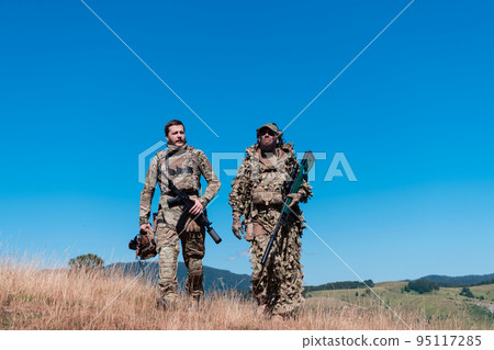 A sniper team squad of soldiers is going undercover. Sniper assistant and team leader walking and aiming in nature with yellow grass and blue sky. Tactical camouflage uniform. 95117285