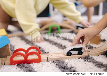 Little boy holds a toy train in hands and rides it on a wooden rail Little boy holds a toy train in hands and rides it on a wooden rail 95117804