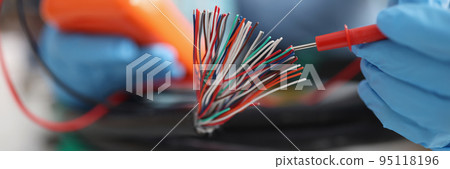 Hands with a voltmeter check colored wires in the cable, blurry 95118196